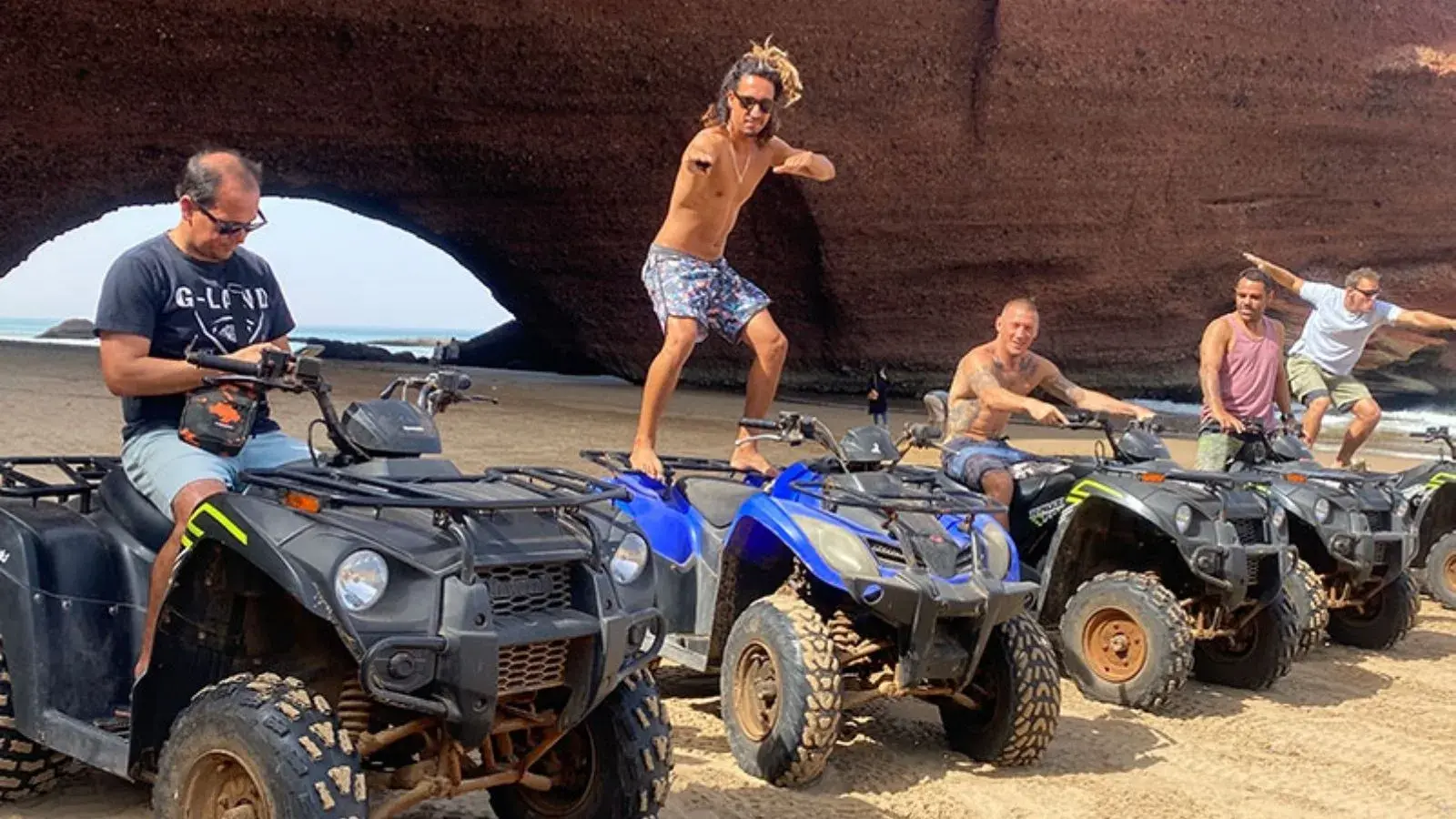 Fem fyrhjulingar på stranden under den röda klippbågen vid Legzira, en förare står på sätet.